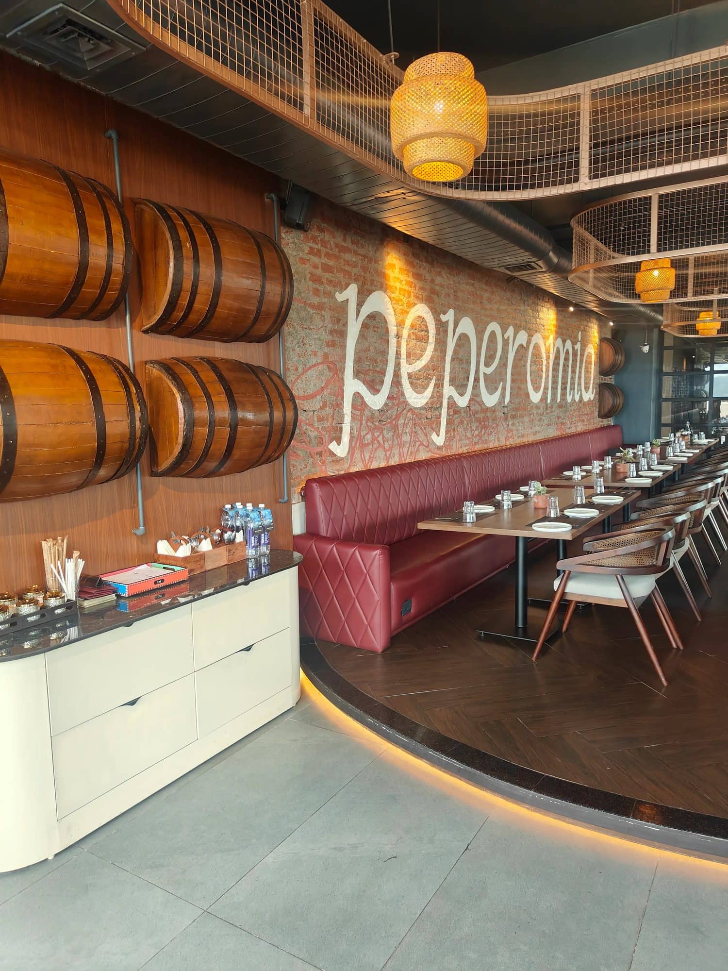 Indoor dining room with the Peperomia logo on a brick wall, barrels and a long table