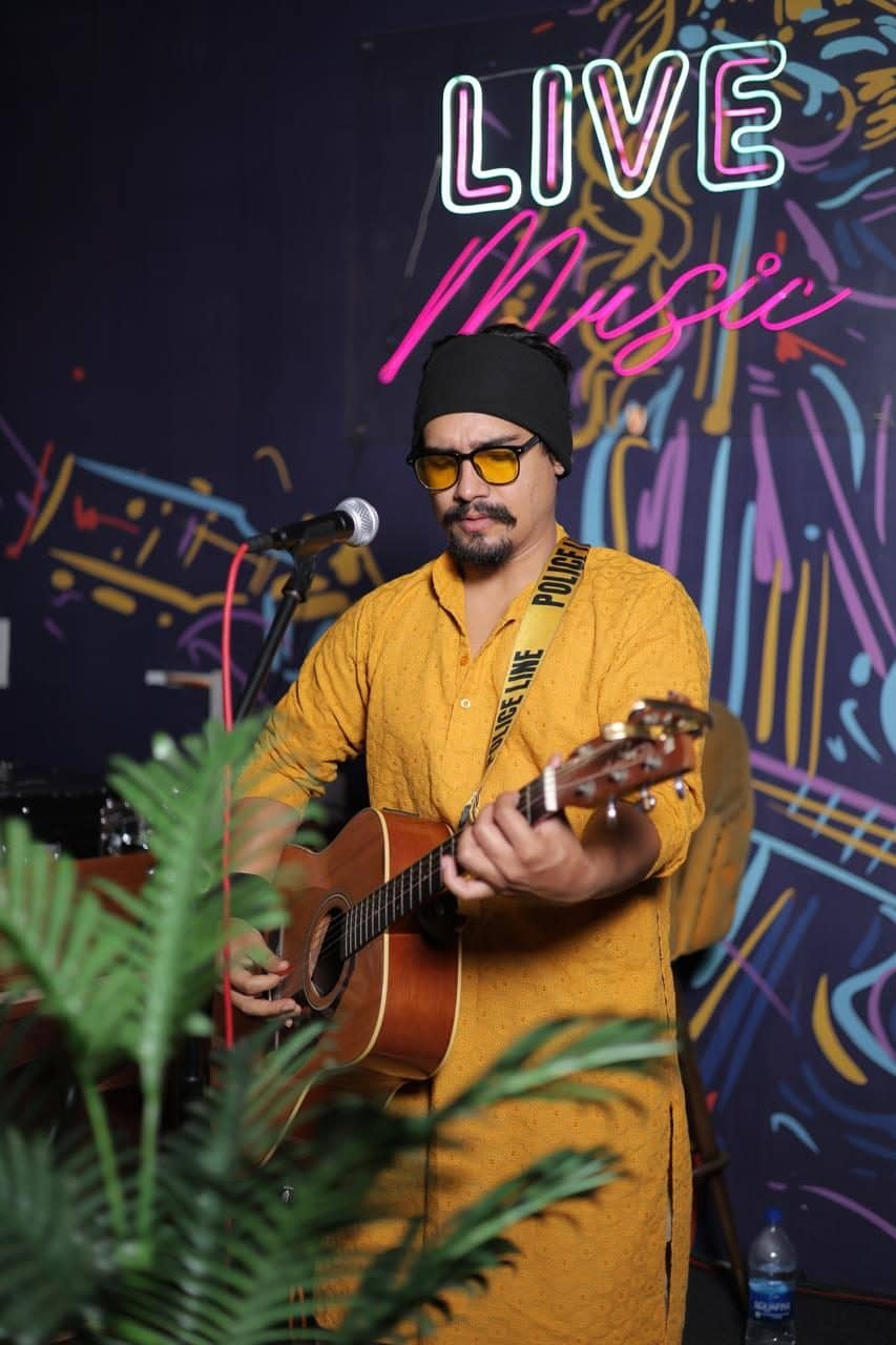 A live singer with a guitar performing in front of a neon live music wall